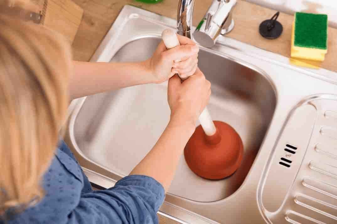 Plumber clearing a blocked sink drain under a kitchen counter in Singapore