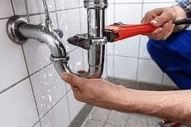 Plumber repairing a leaking pipe behind a wall in a Singapore flat